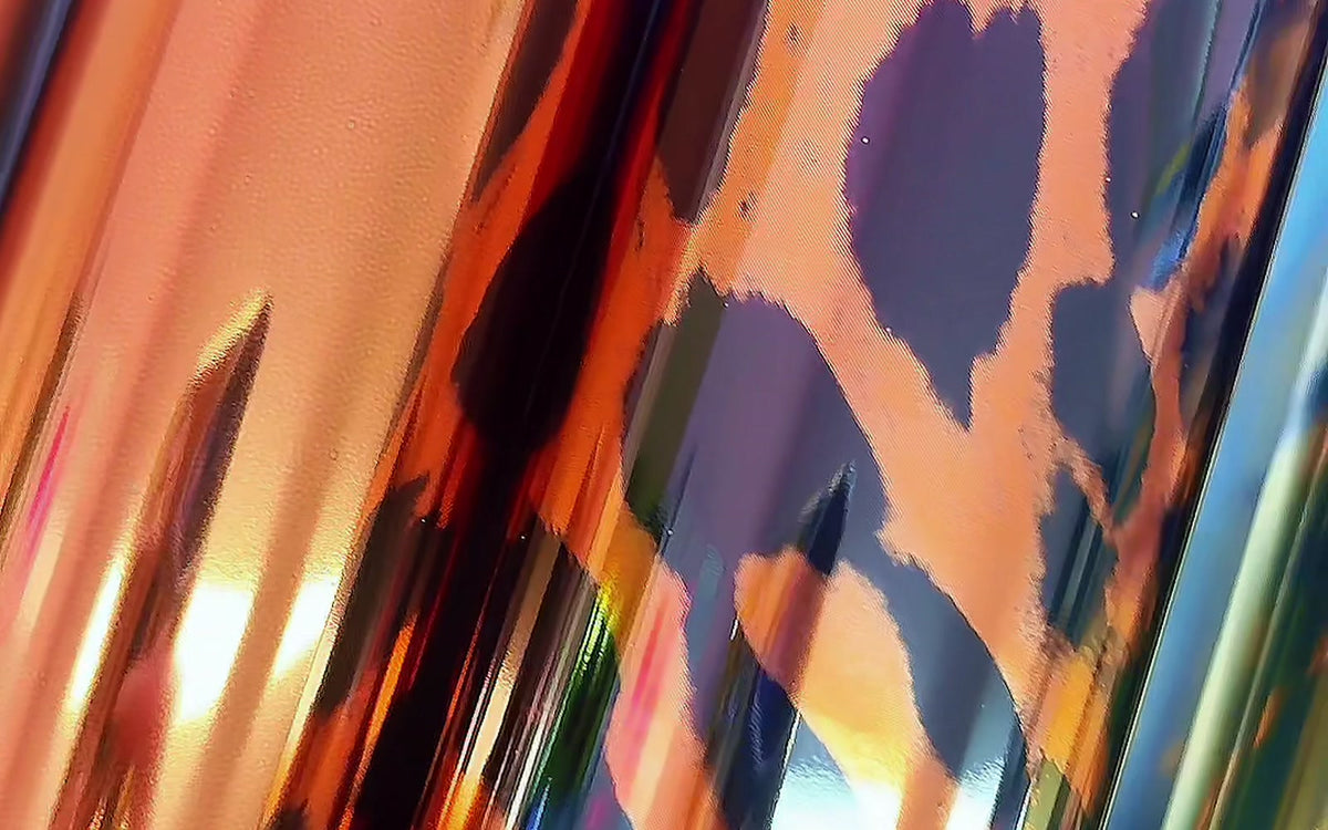 A row of Ugly Betty Confetti toner reactive foil rolls standing side by side, copper, leopard print and blue holographic catching the light
