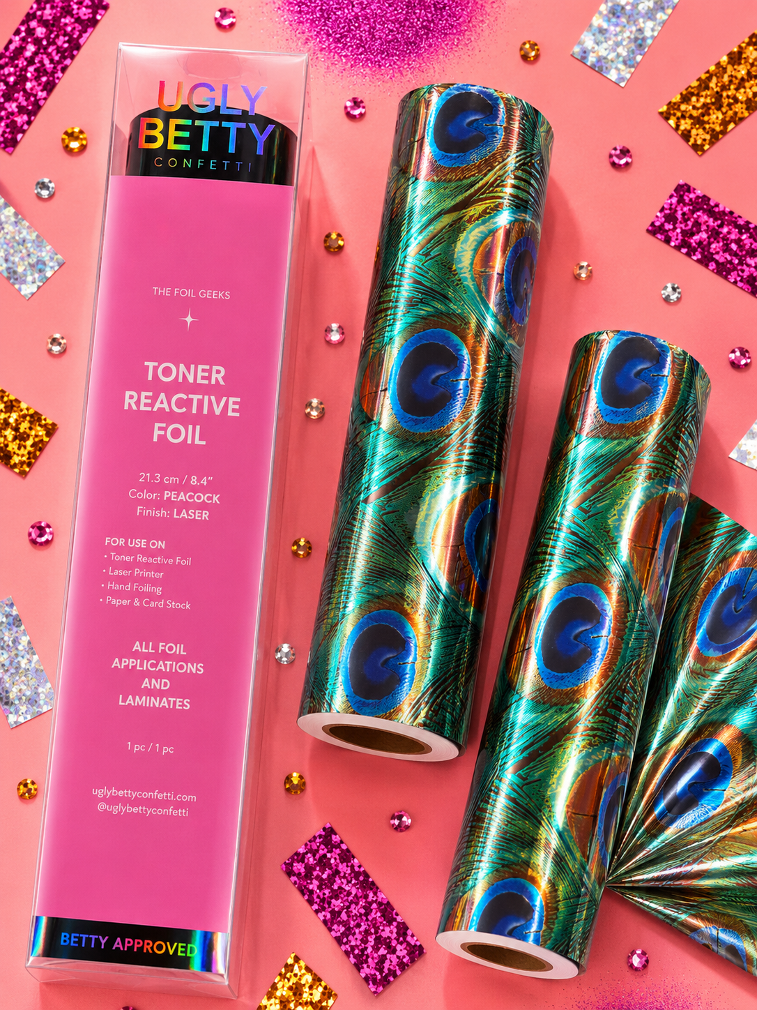 Ugly Betty Confetti Toner Reactive Foil set with a pink retail box and three rolls of shimmering peacock-patterned foil, arranged on a pink background with scattered glitter and confetti.