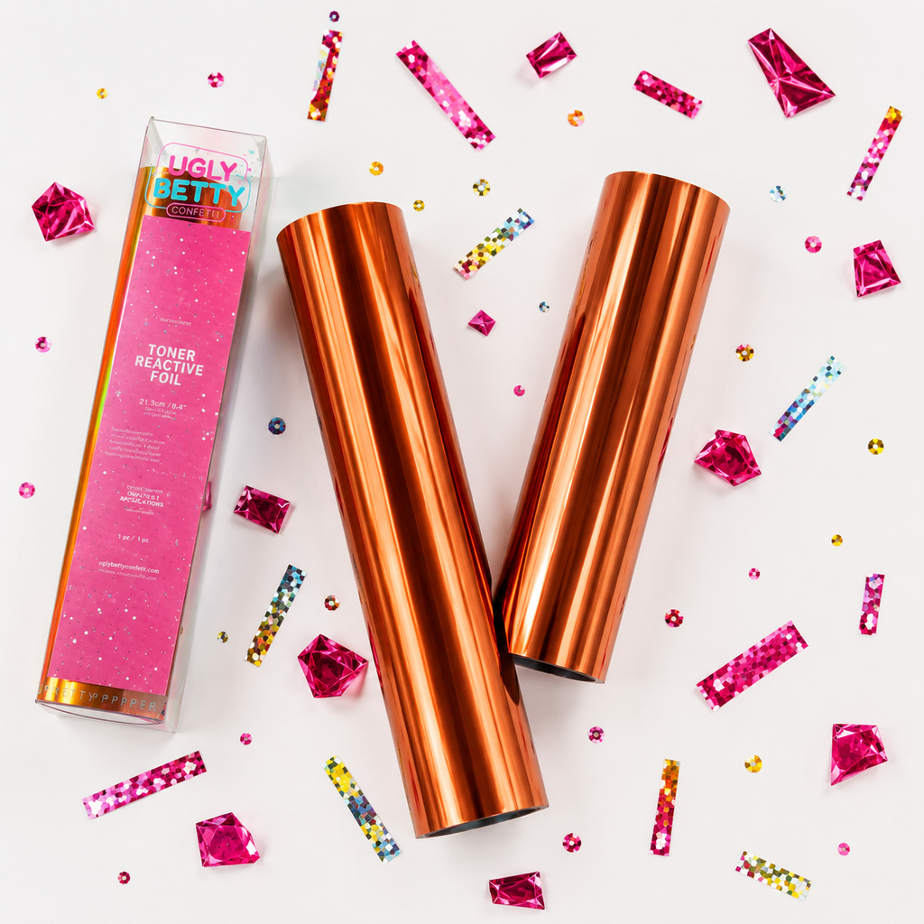 Two copper-toned cylindrical containers with a pink box labeled 'Ugly Betty' on a white background with colorful confetti.
