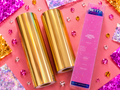 Gold foil rolls and a pink packaging box labeled 'Ugly Betty' on a colorful background with glitter.