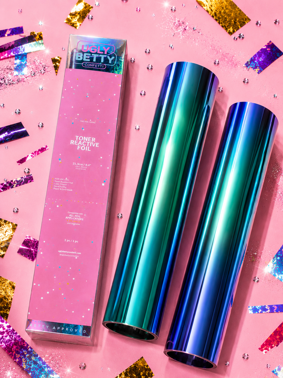 Two iridescent bottles and a pink box with ugly Betty' branding on a pink background with confetti.