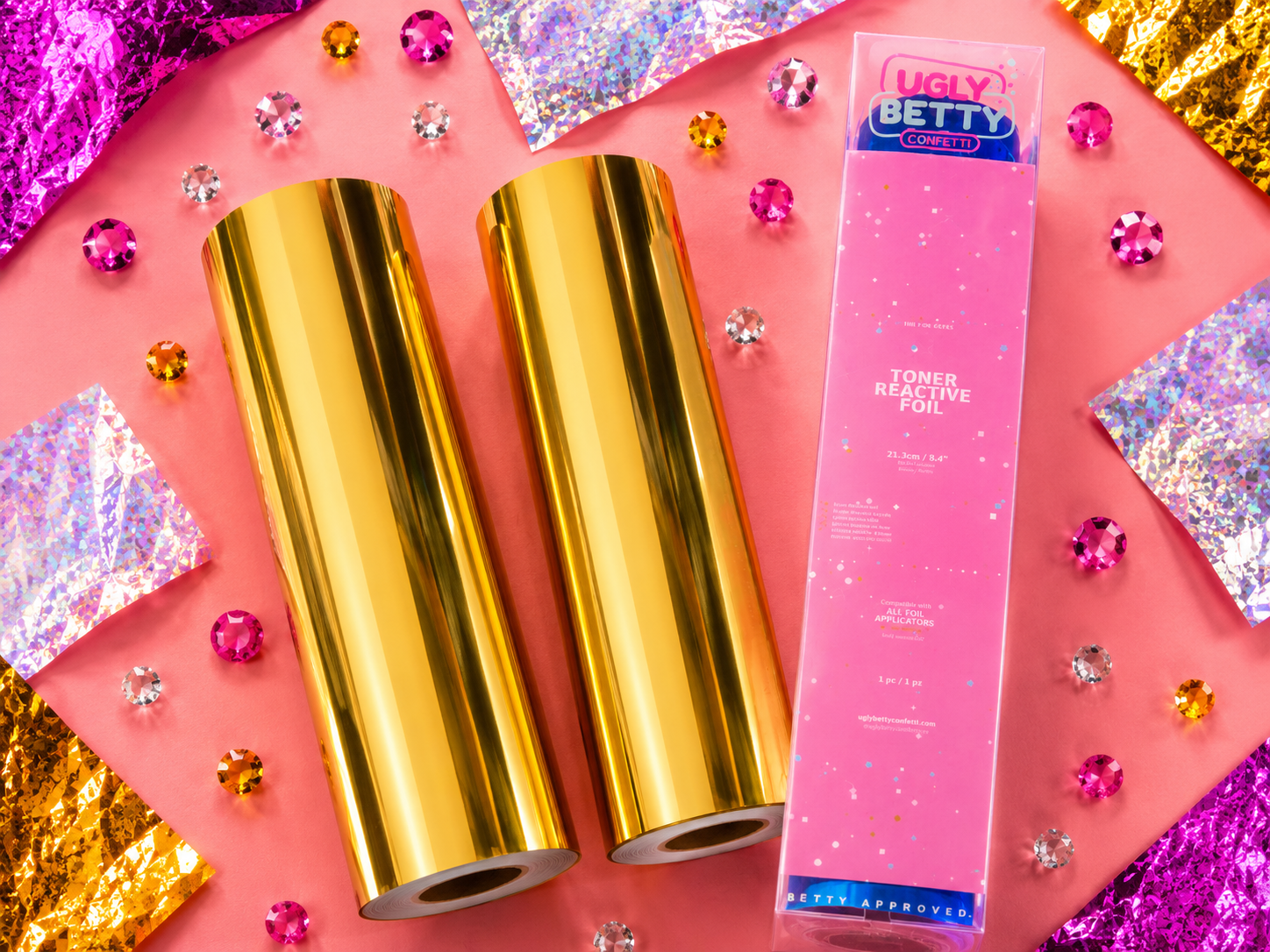 Gold foil sheets and a pink box labeled 'Ugly Betty' on a colorful background with glitter.