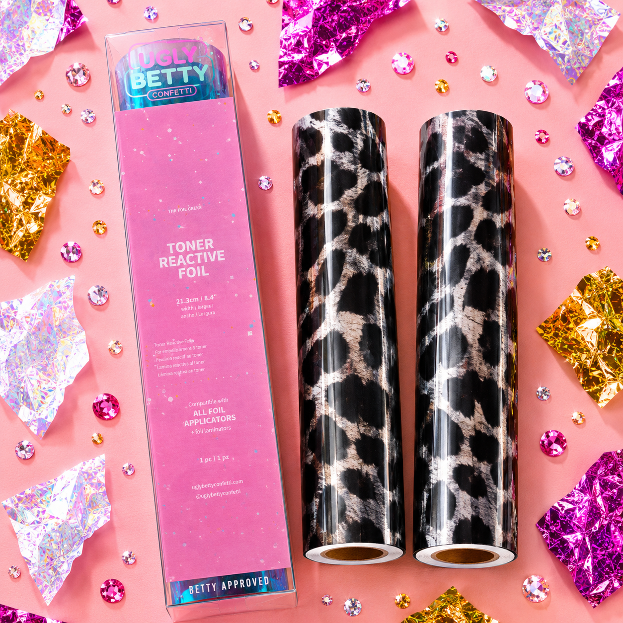 Two toner reactive foil rolls with a pink box on a decorative background with glitter and confetti.