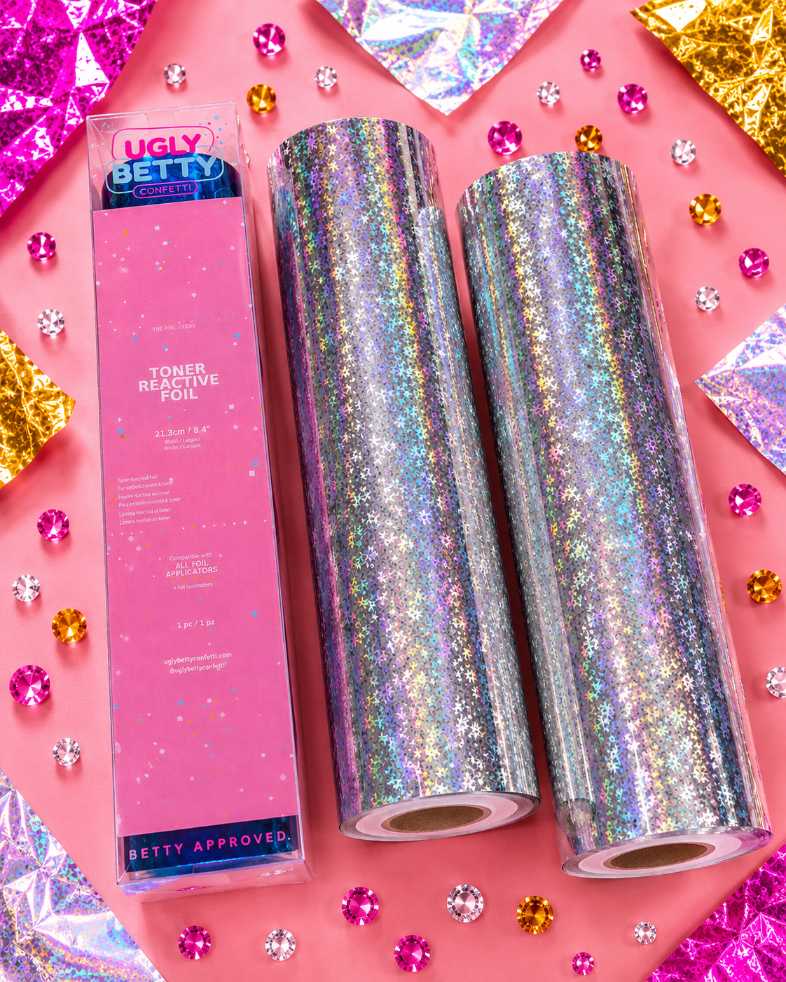 Two rolls of iridescent toner reflective foil with a pink box labeled 'Ugly Betty' on a pink background with decorative elements.